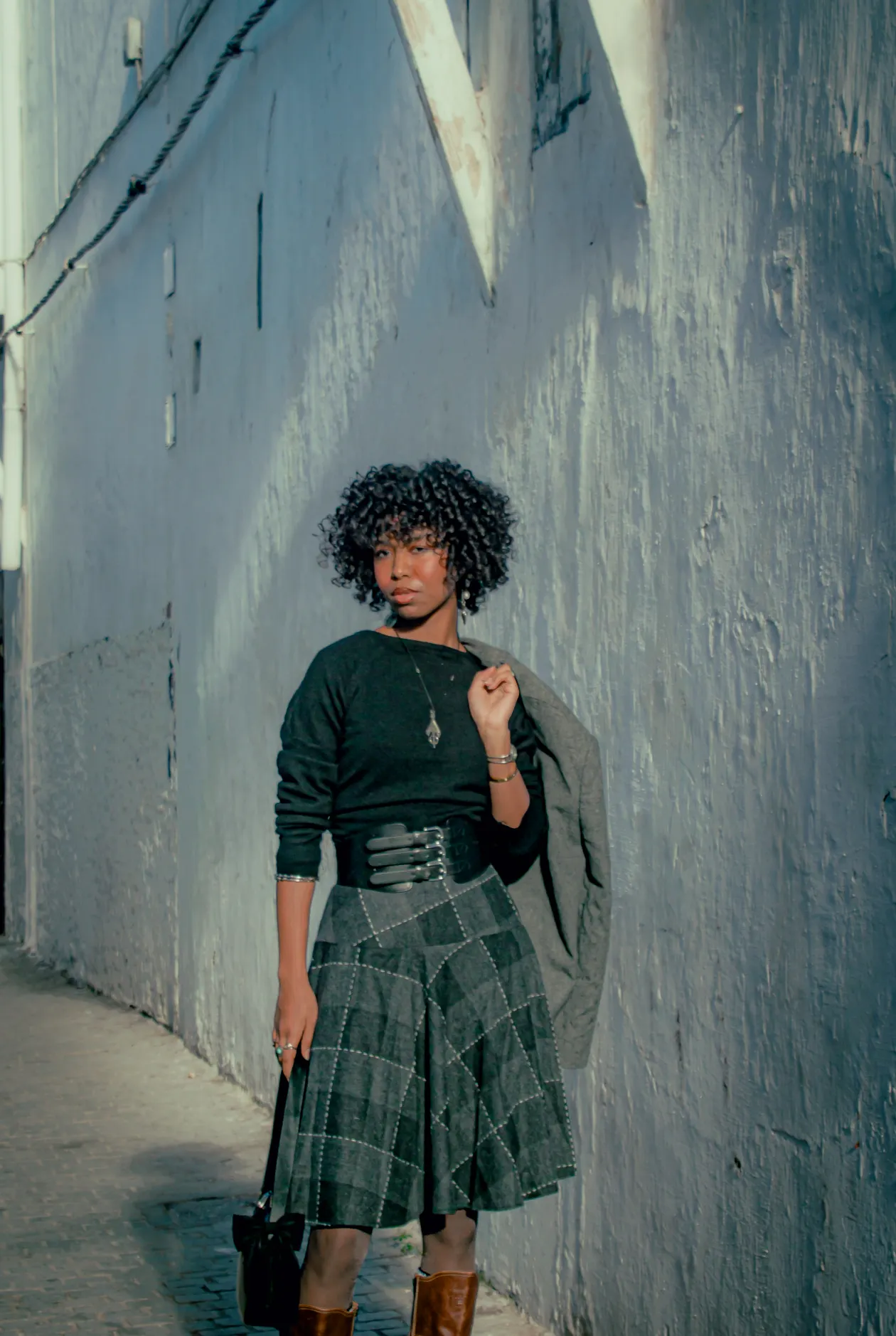 Woman in a belted dress with a plaid skirt in a street setting