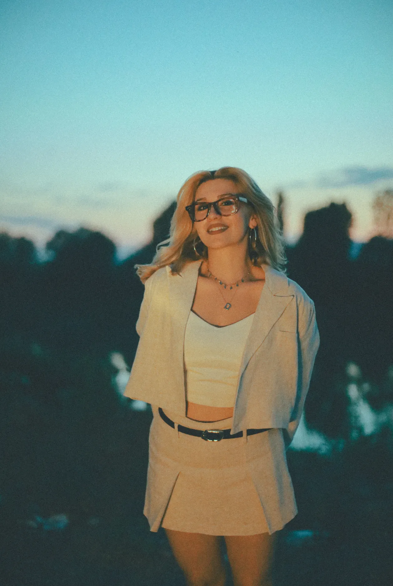 Woman in a belted blazer outdoors at dusk