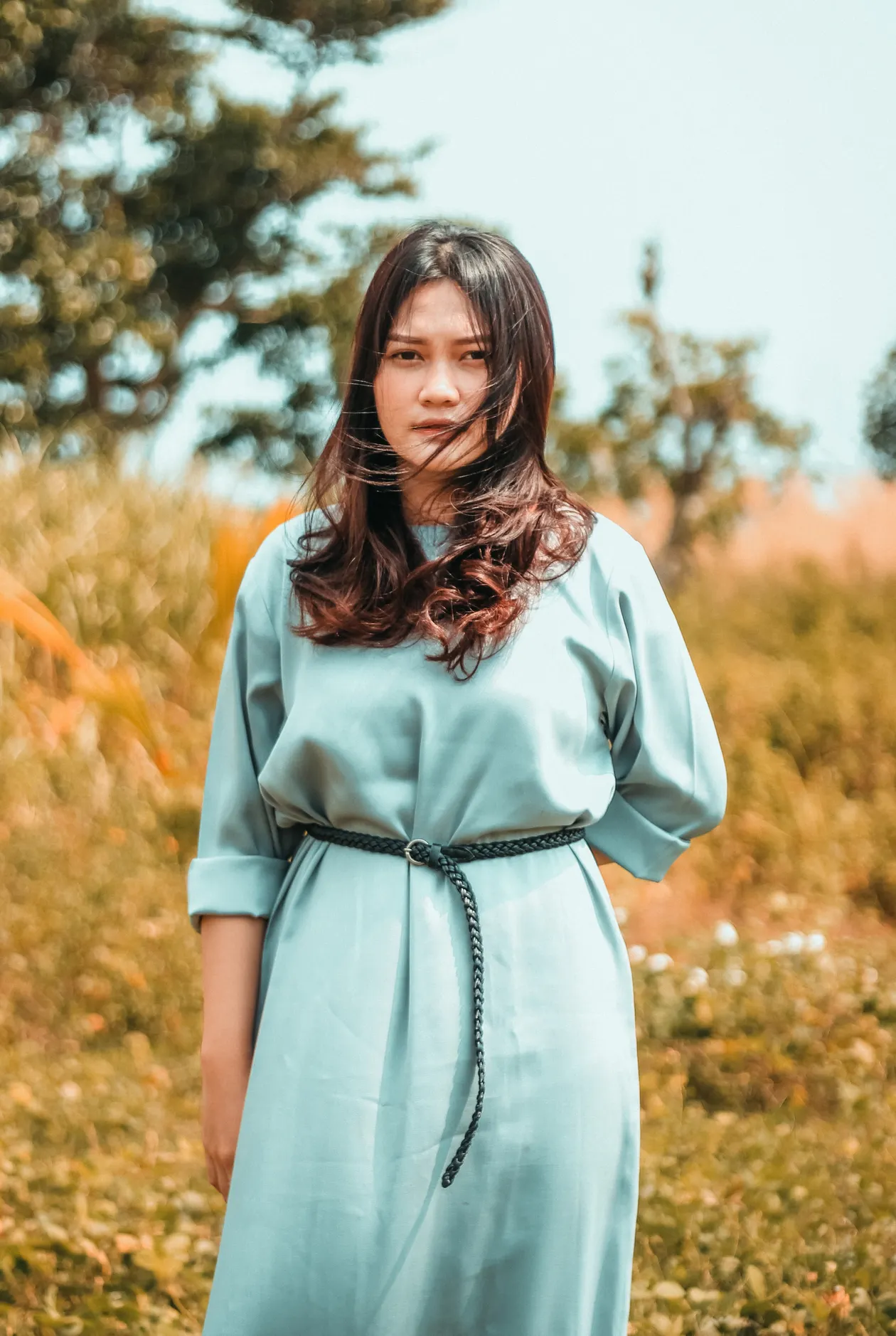 Woman in a blue belted dress outdoors in greenery