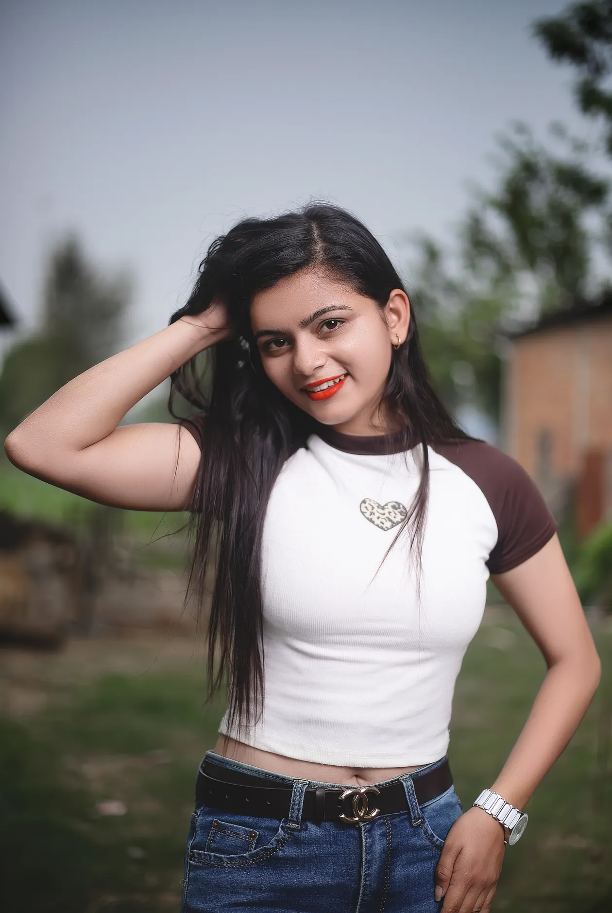 Woman in a white top with brown raglan sleeves, blue jeans, and a black belt with a gold double-C buckle.