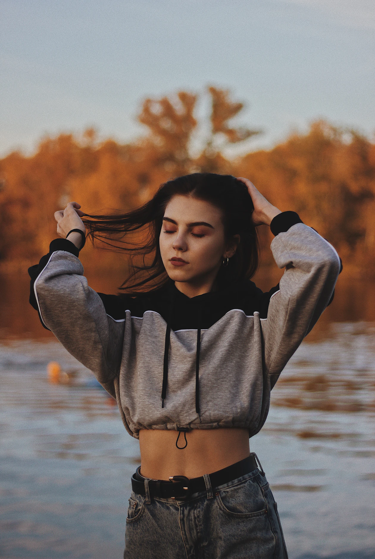 Woman in a grey and black cropped hoodie, blue grey jeans, and a black belt.