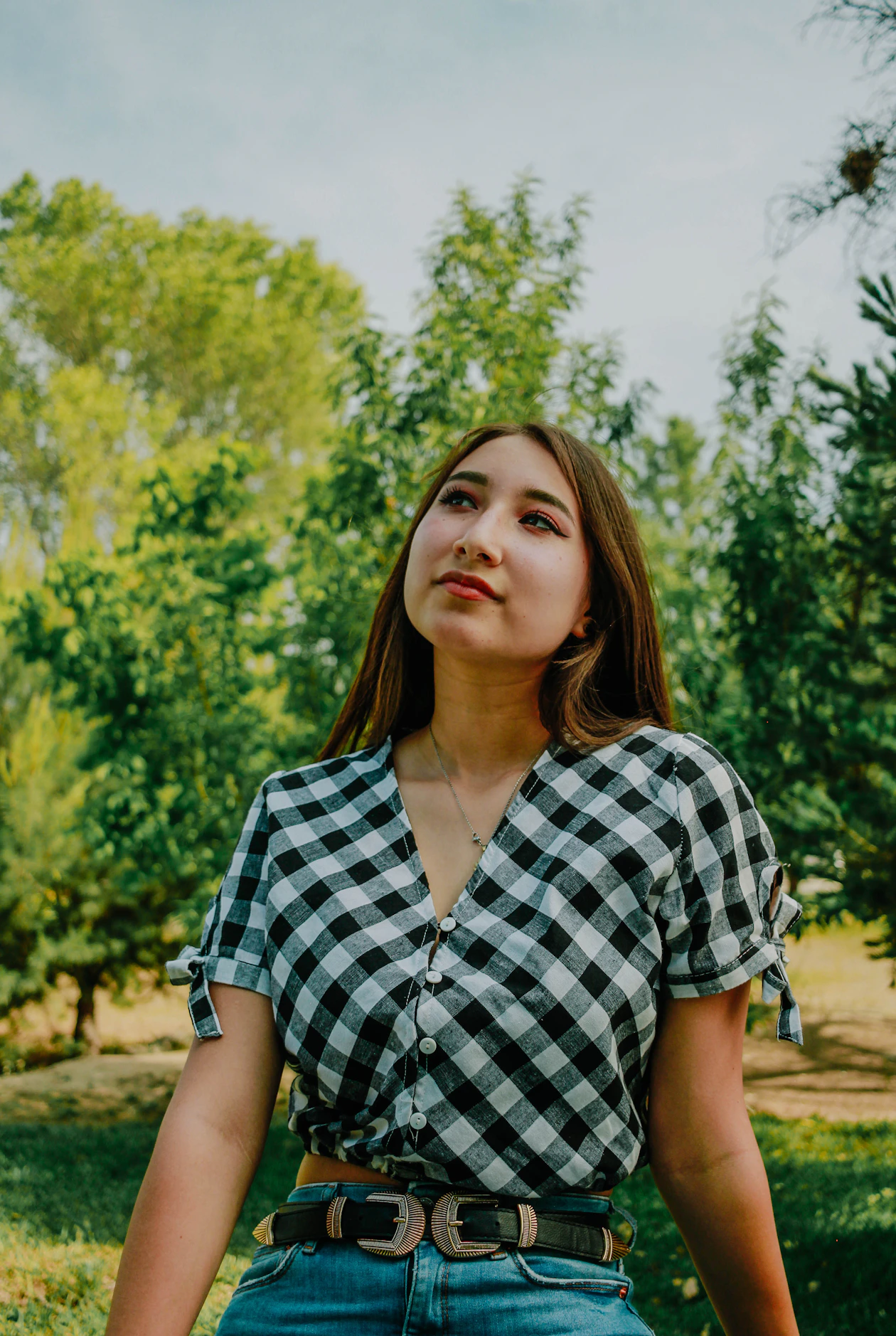 Woman in a black and white checked shirt, blue jeans, and a black belt with a large double buckle.